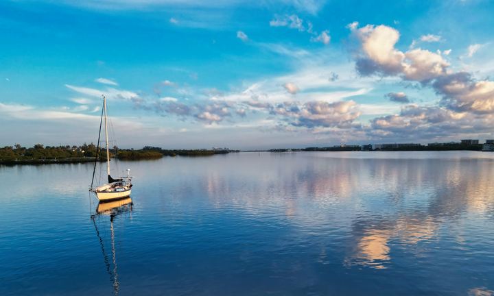 Sailboat anchored on a calm Florida lake with cumulus reflections