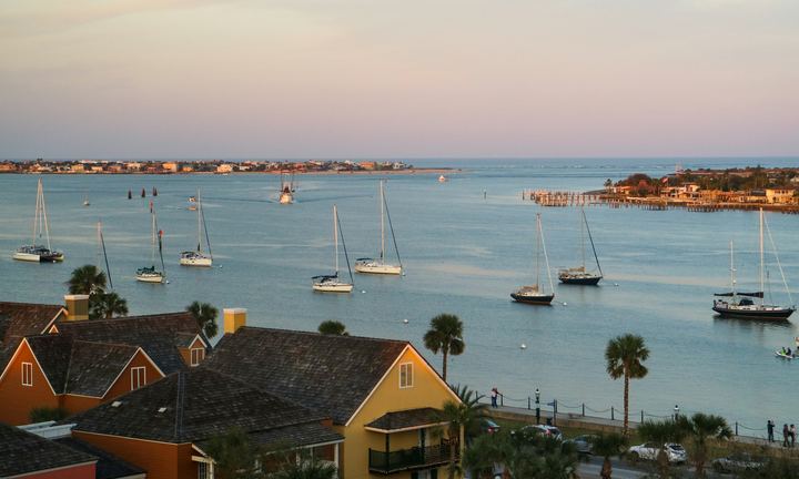 Sailboats anchored in St. Augustine harbor at golden hour with historic rooftops and palms